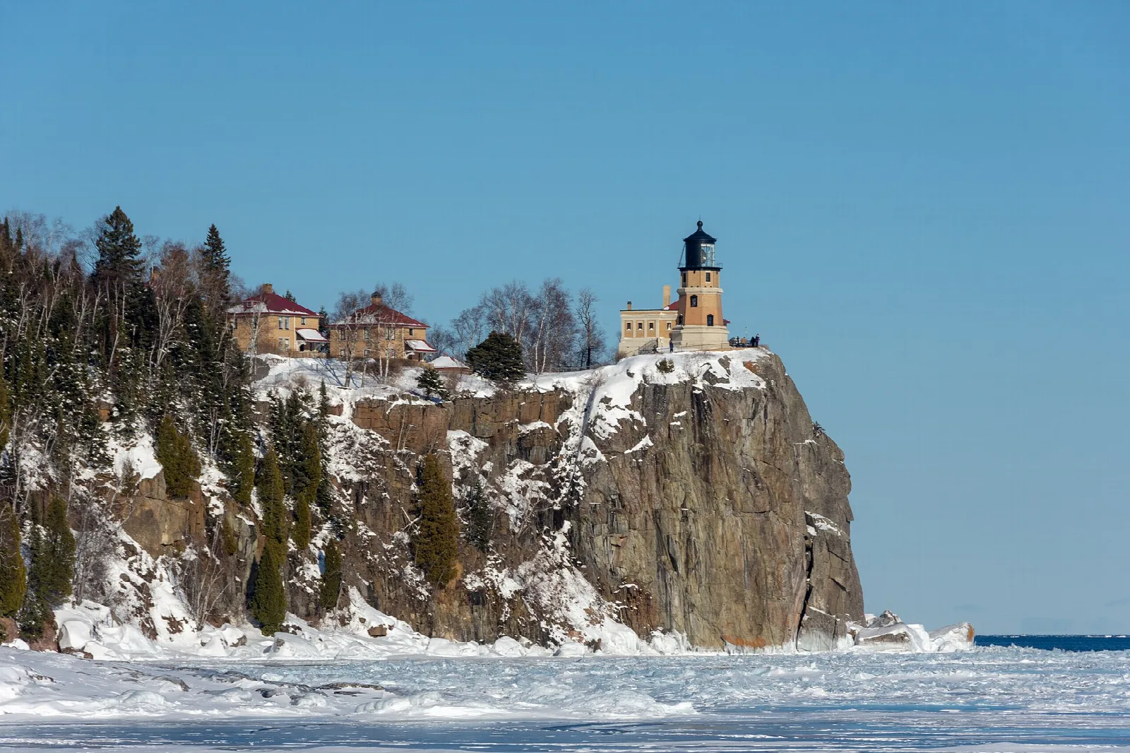 Lighthouse on a snowy cliff with evergreens and blue sky