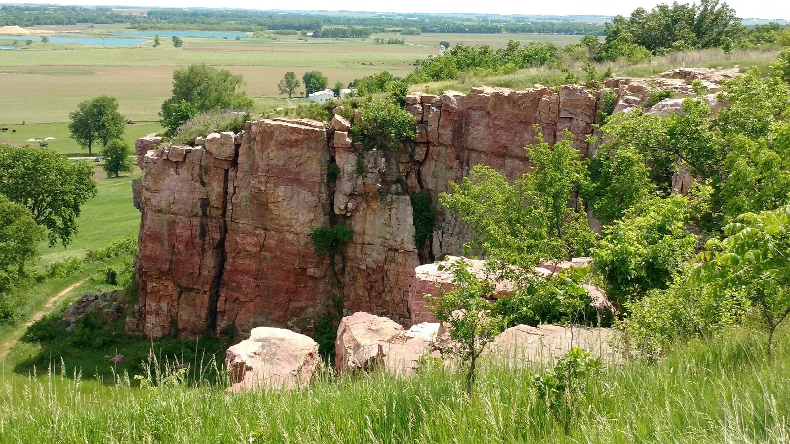 Pink quartzite cliff rising from green prairie with farmland beyond