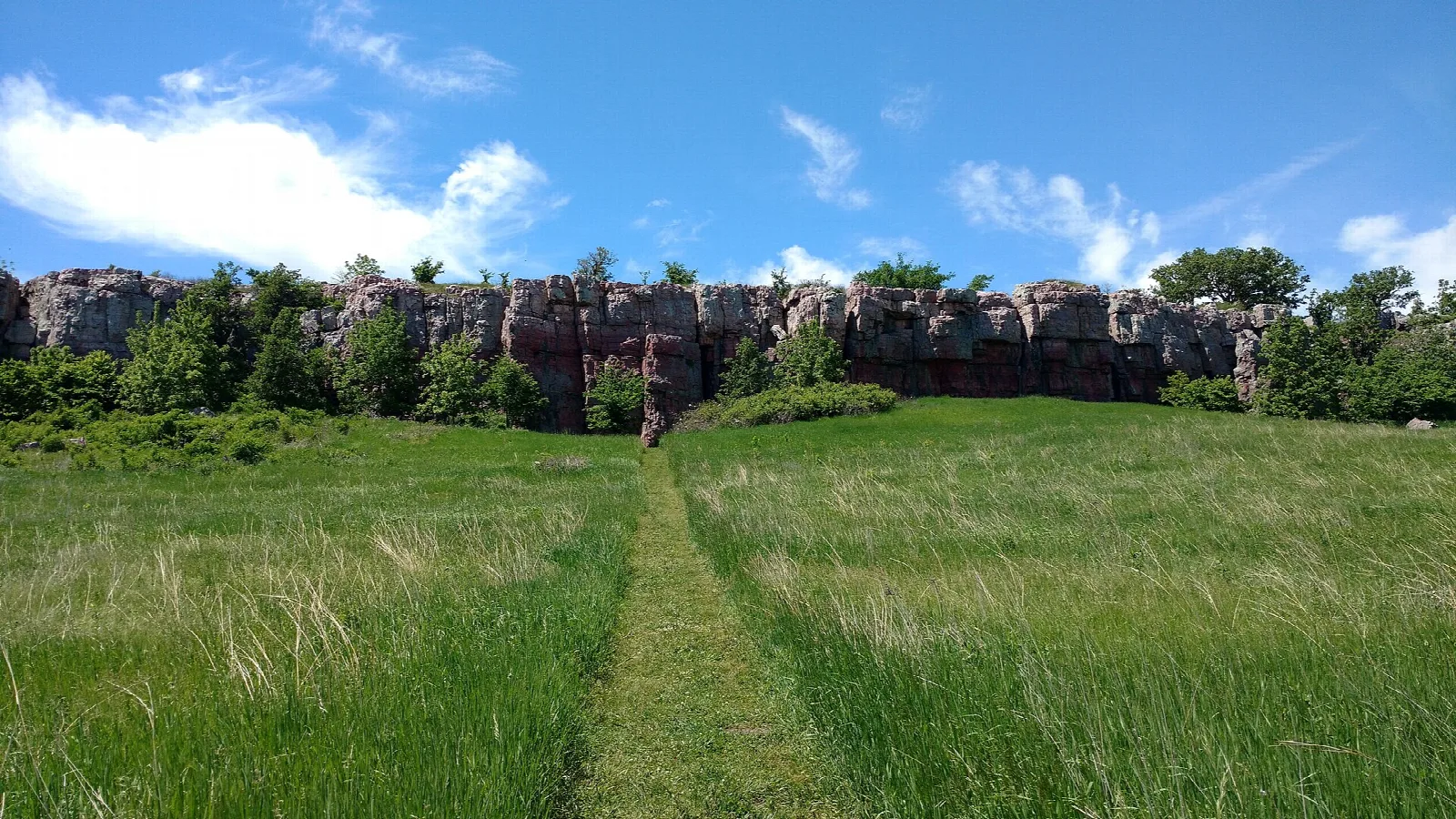 Mown path through grass leading toward a line of rock cliffs