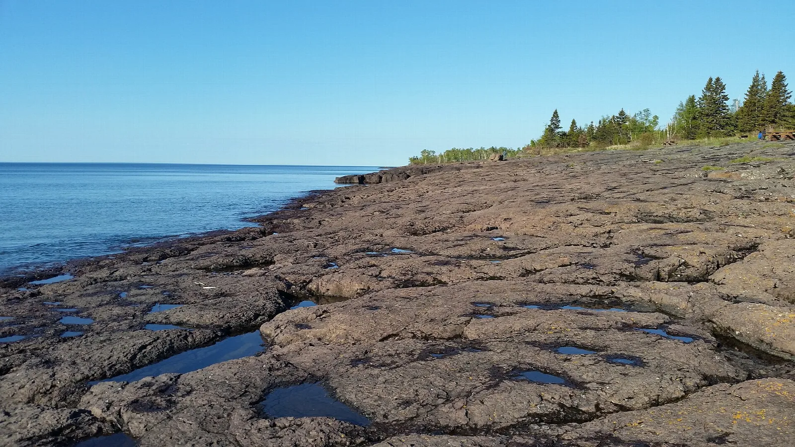 Flat rock shelf with small pools beside a wide blue lake