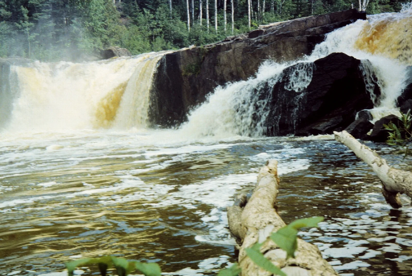 Brown river water tumbling over a rocky ledge in a waterfall