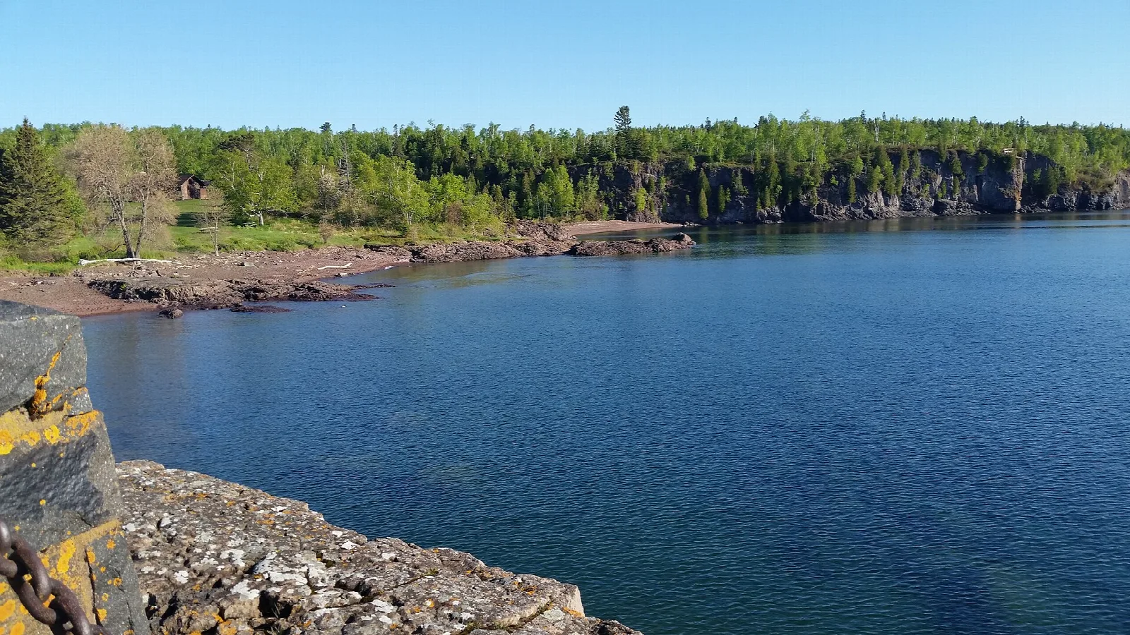 Blue lake bay with a rocky shore and forested cliffs
