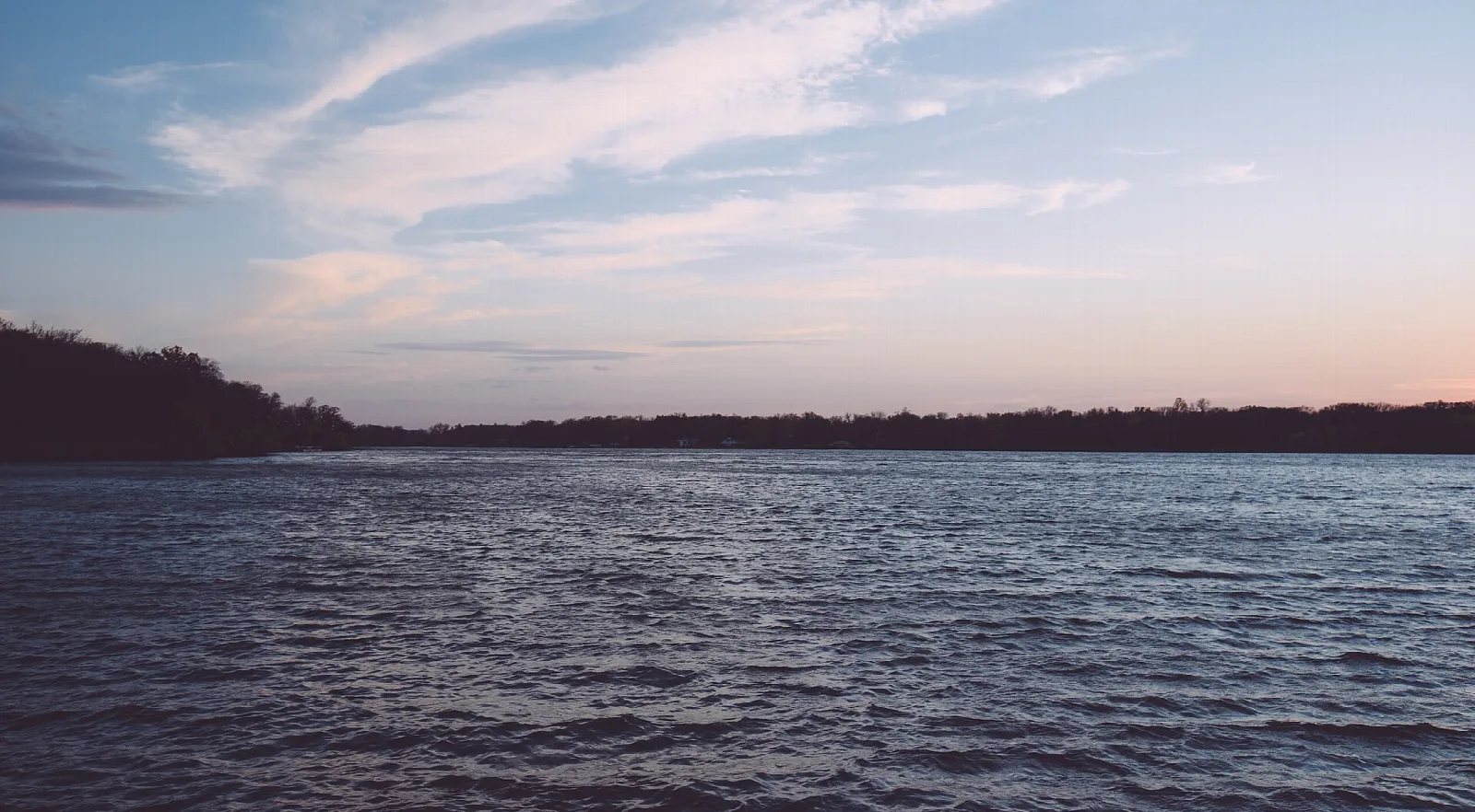 Wide lake with dark shoreline under a pink sunset sky