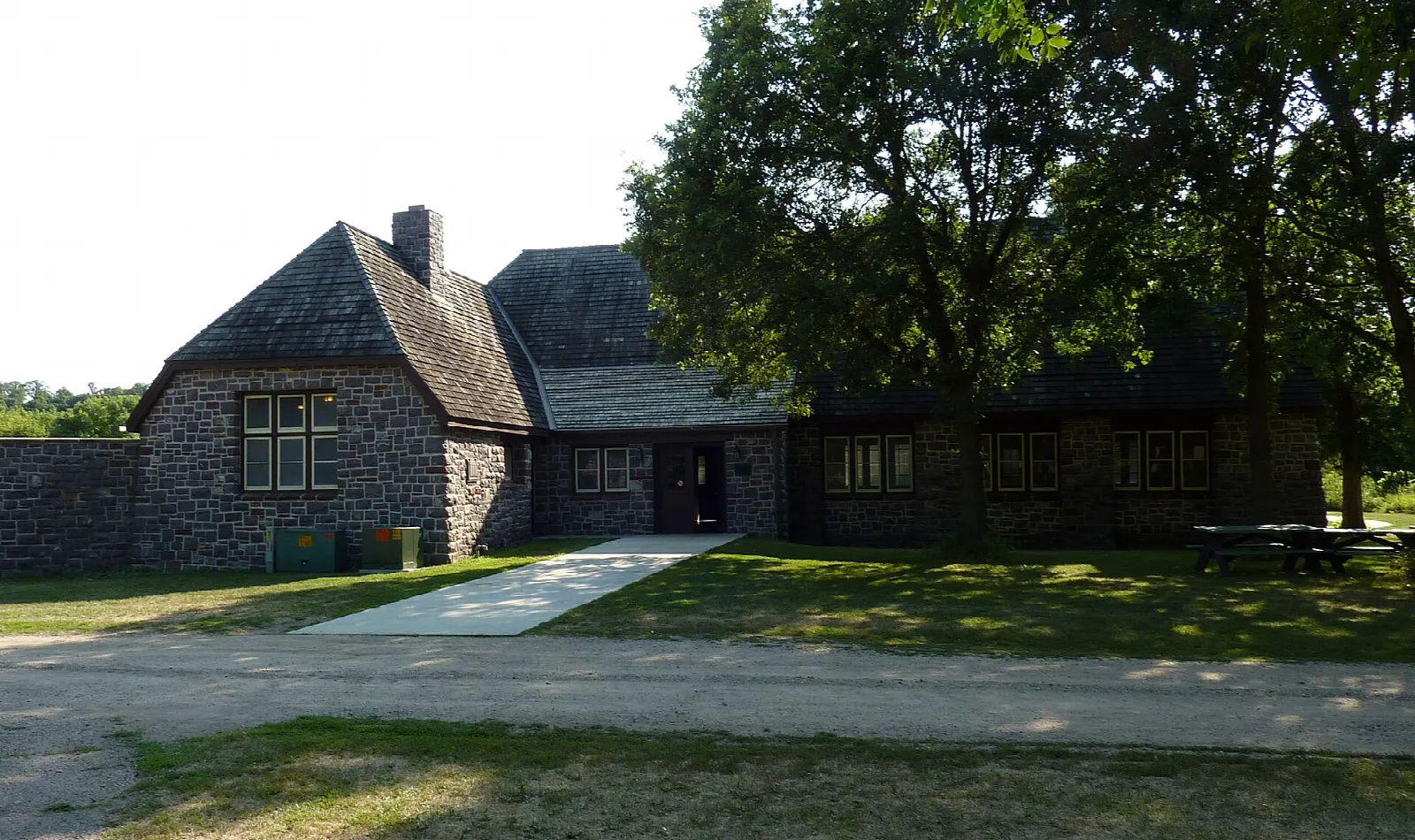 Stone building with a steep roof under large trees