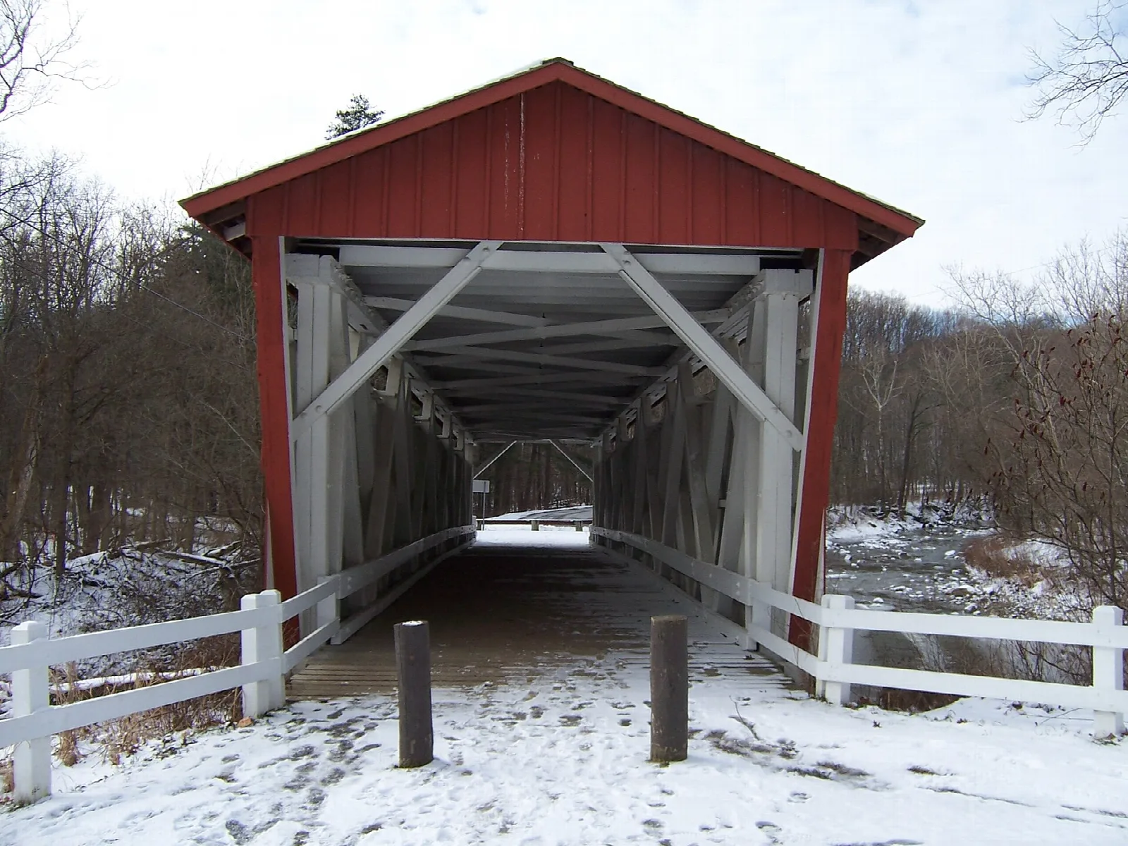 A red covered bridge with white fencing in a snowy landscape