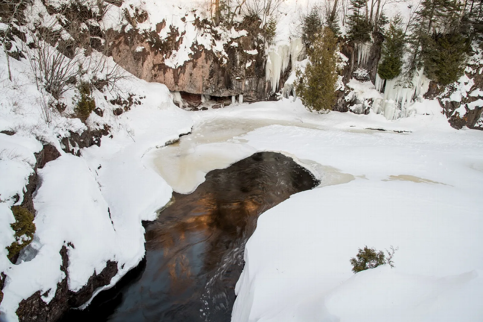 Snowy gorge with a dark pool of water between rock walls