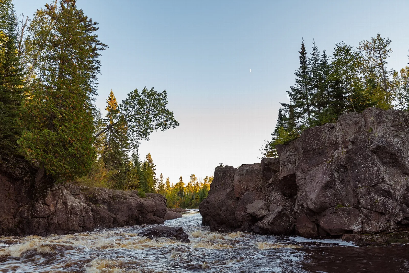 River passing between dark rocks and spruce trees at dusk