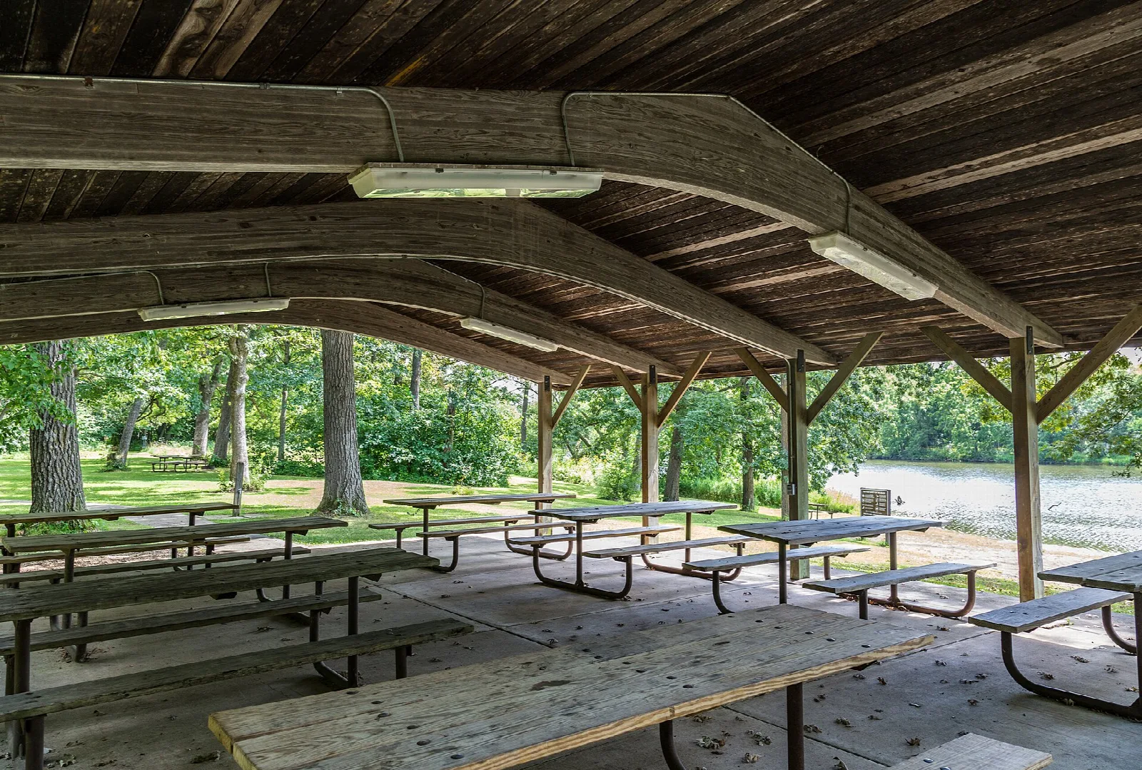 Open picnic shelter with many tables and a lake behind