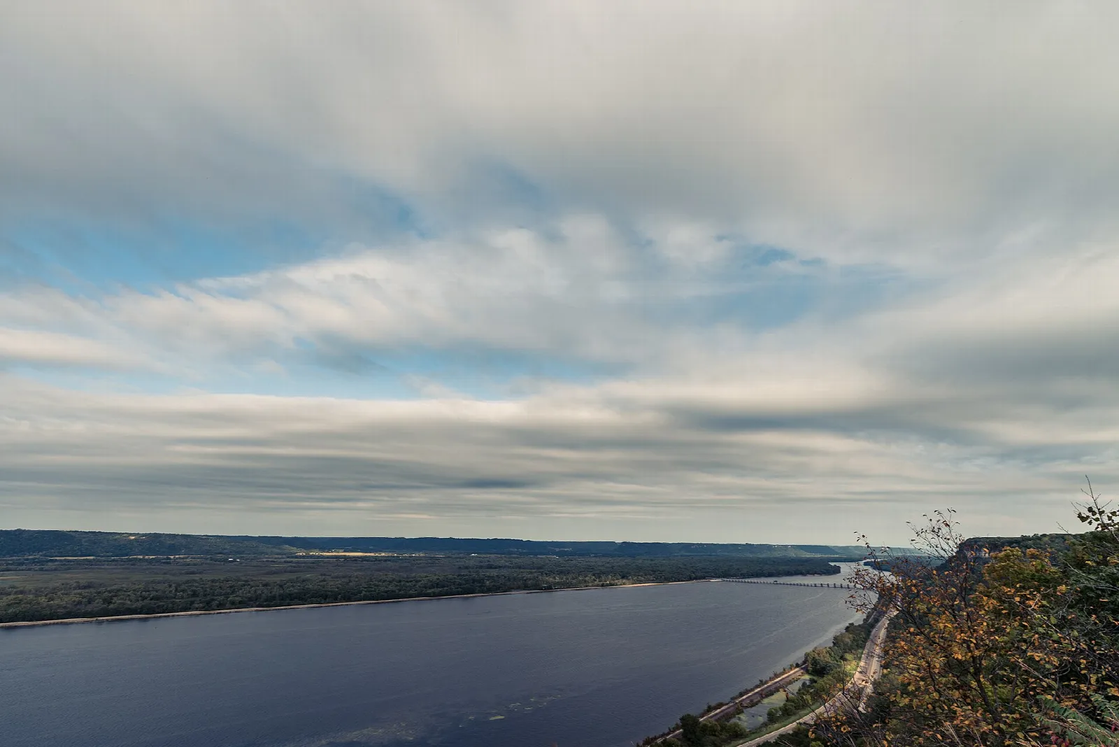 Wide river under a cloudy sky with a wooded bluff on the right