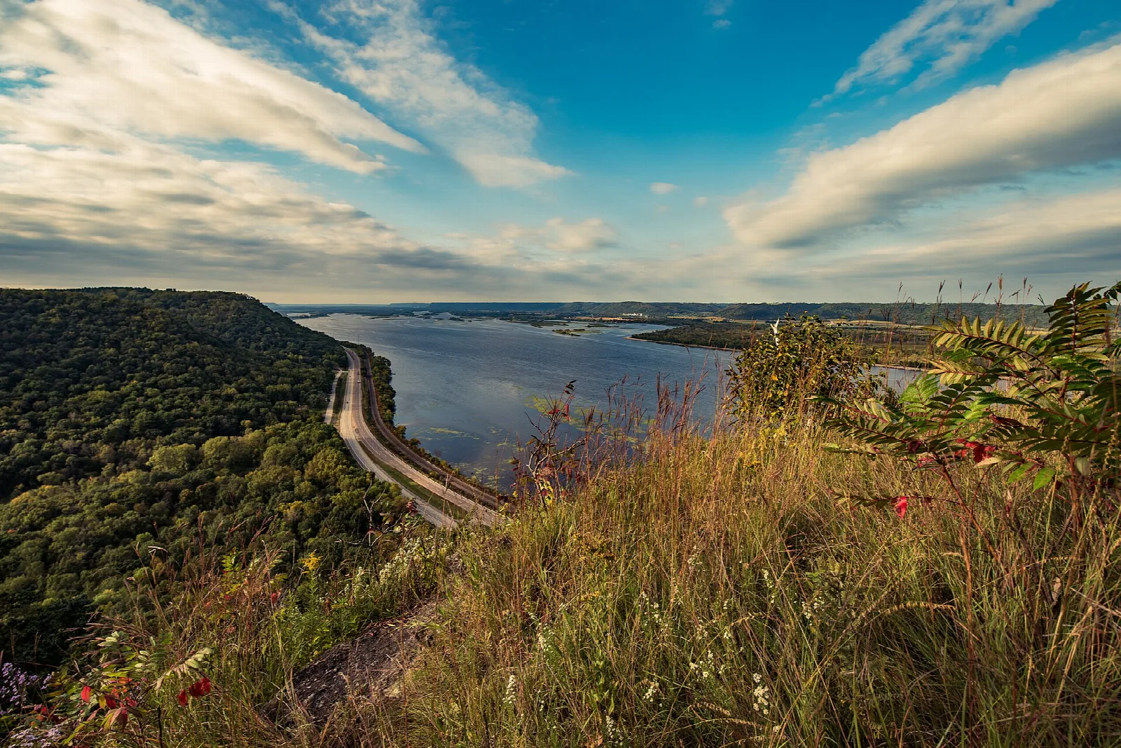Wide river and a road below a forested bluff, seen from a high overlook