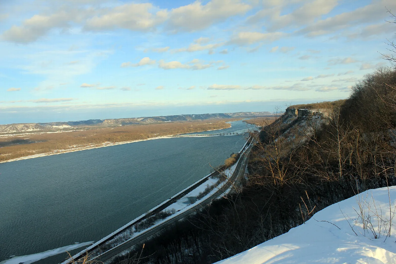 River bending below a steep bluff with snow on the ground