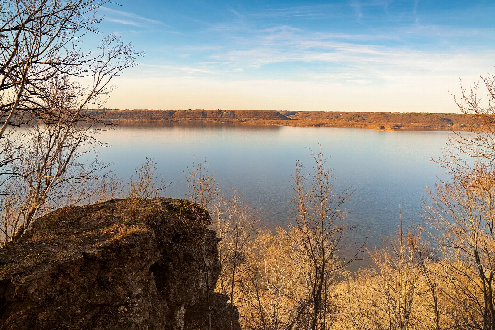 Wide blue lake seen from a limestone bluff with a rock outcrop in the foreground