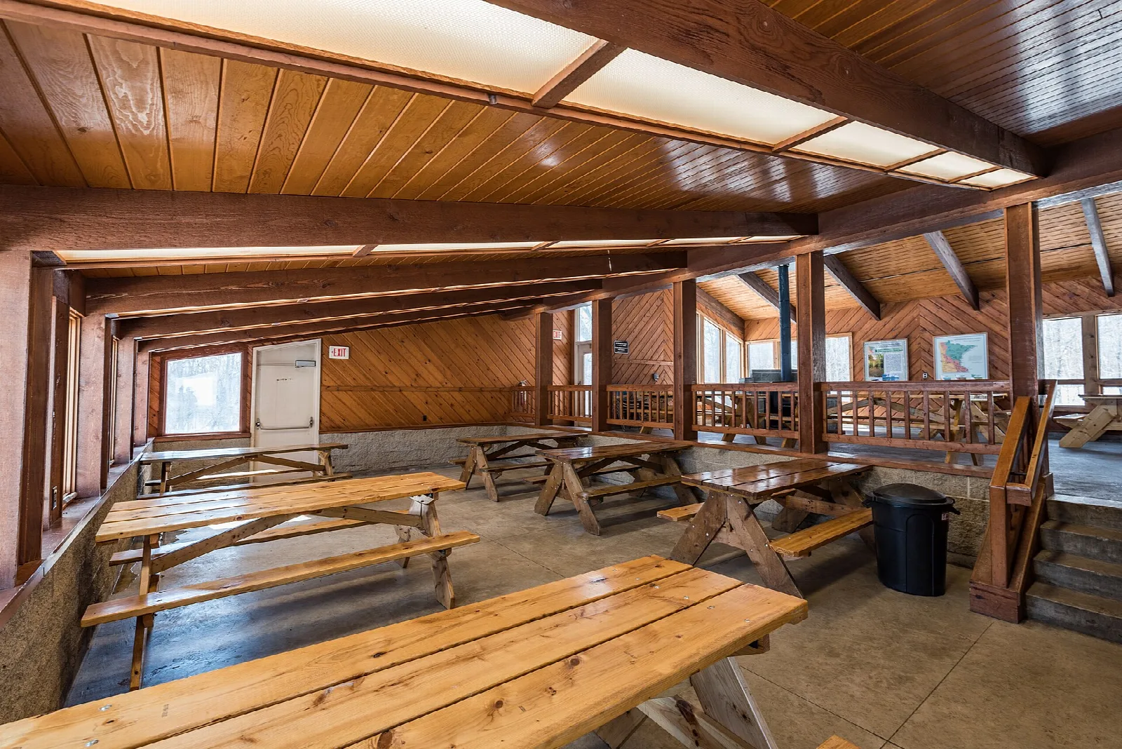 Inside an open lodge with wooden picnic tables and a wood ceiling