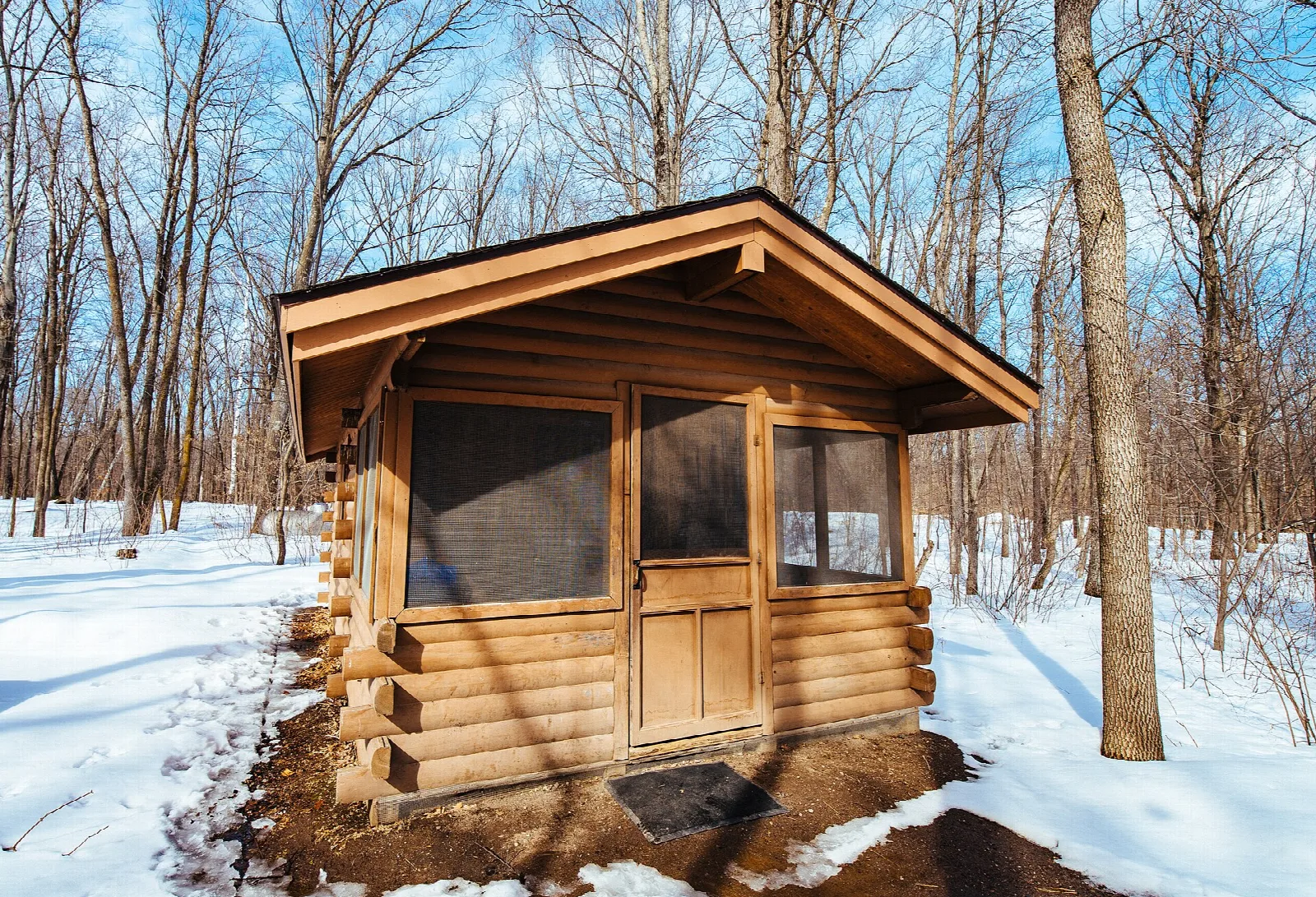 Small log camper cabin with a screen door in a snowy wood