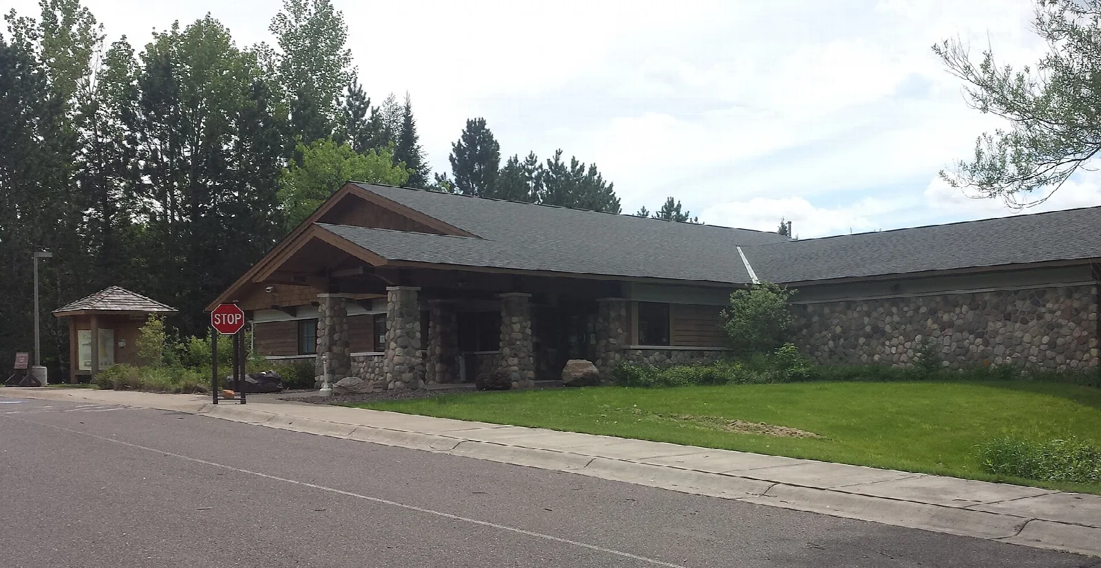 Low stone and wood building with a gabled entrance beside a road