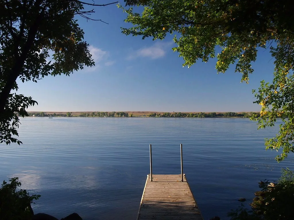 Wooden dock extending into a calm wide lake under blue sky