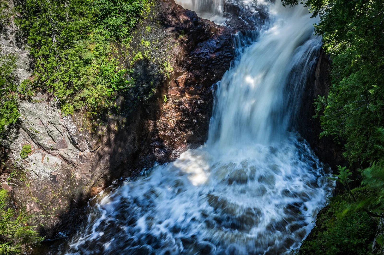 Waterfall pouring down a rock face edged with green plants