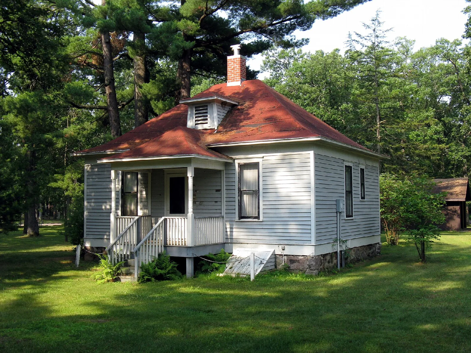 Small white house with a red roof and porch on a lawn