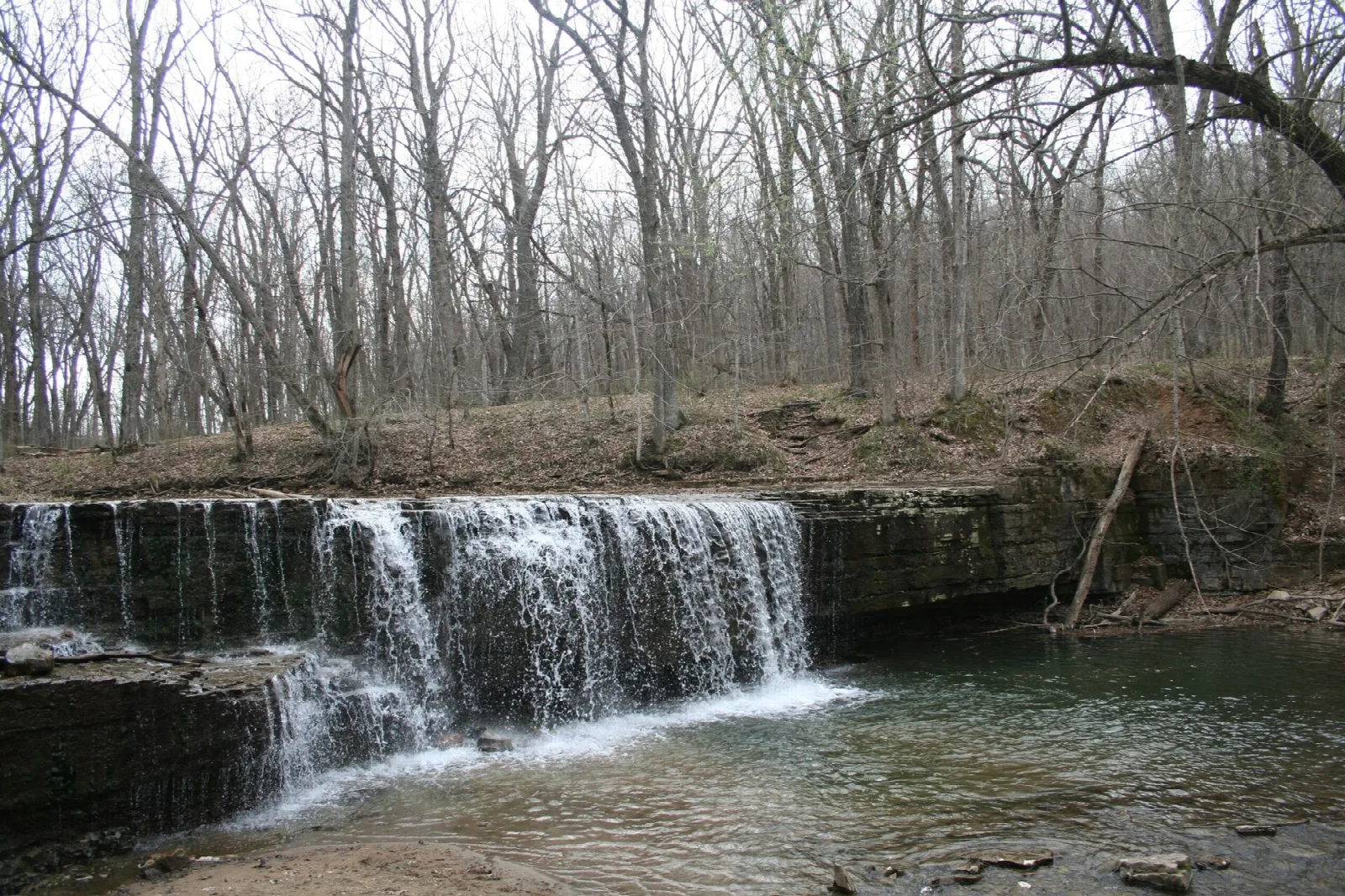 Waterfall over a rock shelf into a creek in bare spring woods