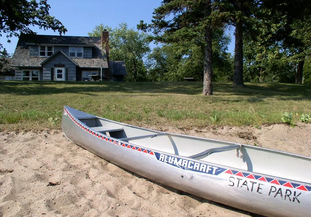 Canoe on a sandy beach with a log building behind
