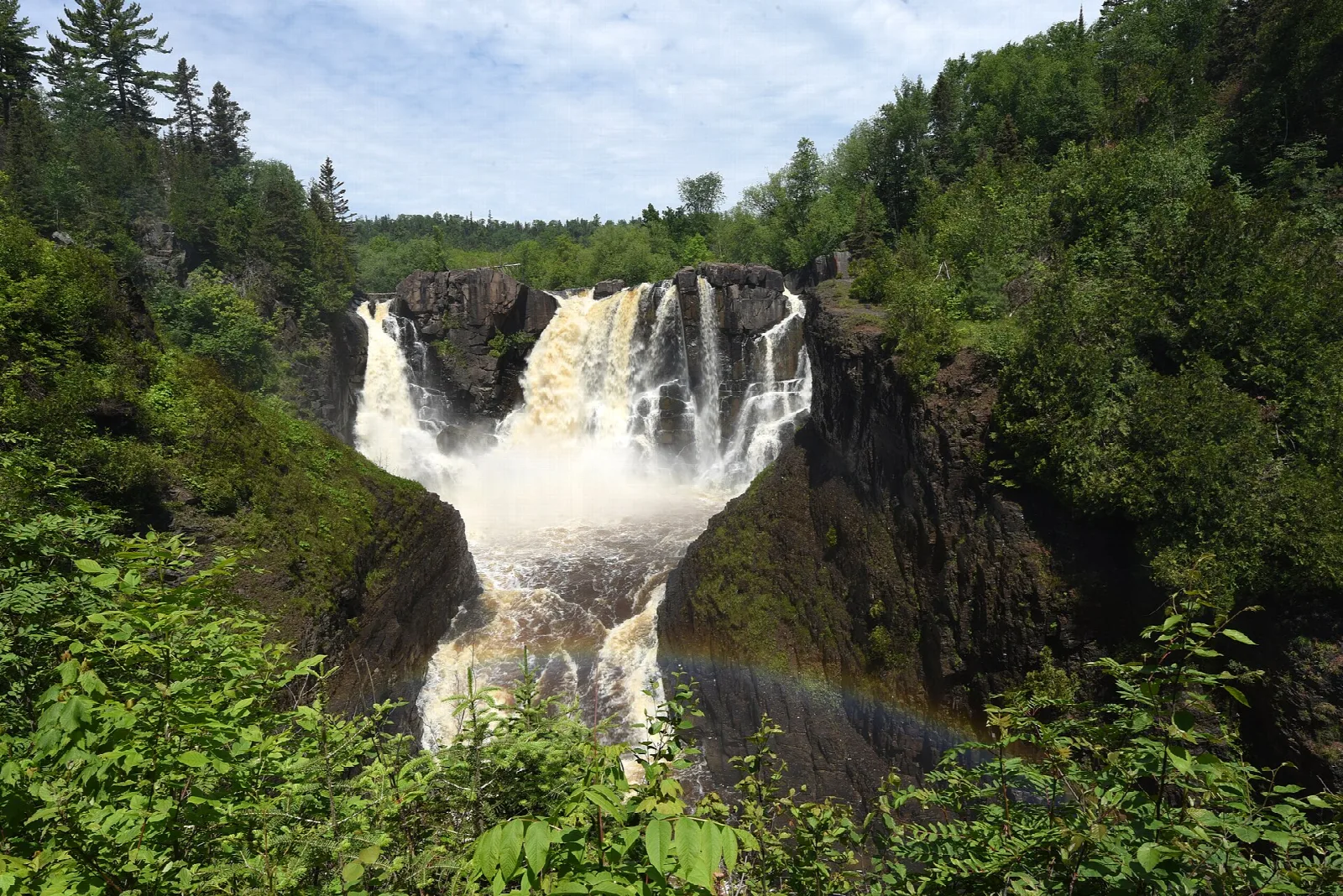 Large waterfall dropping between dark cliffs and green forest