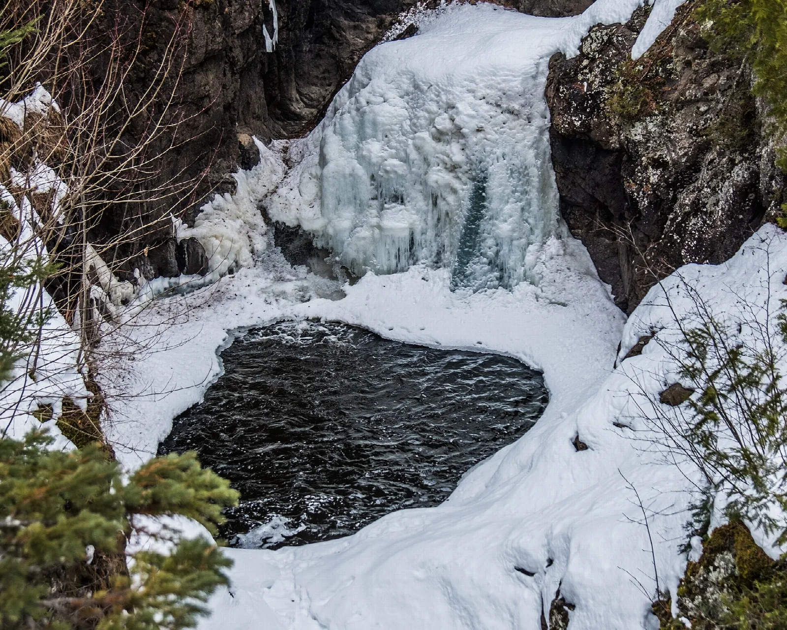 Frozen waterfall above a dark pool in snow