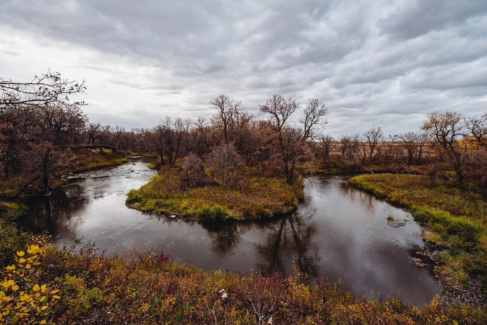 River winding through grassland with autumn color under cloudy sky