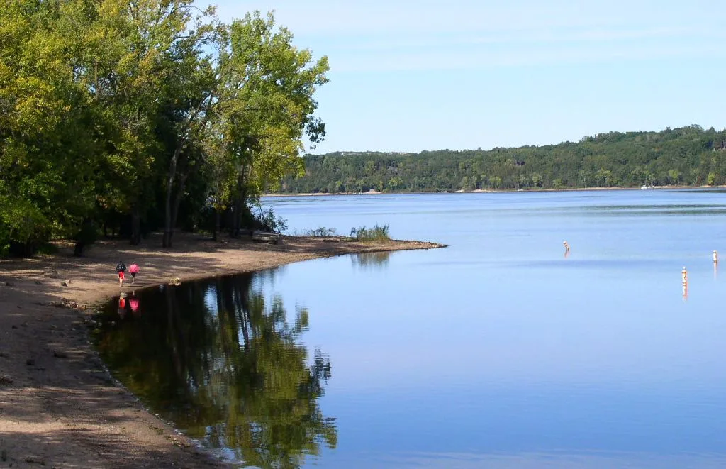 Sandy river shore and calm water with wooded hills beyond