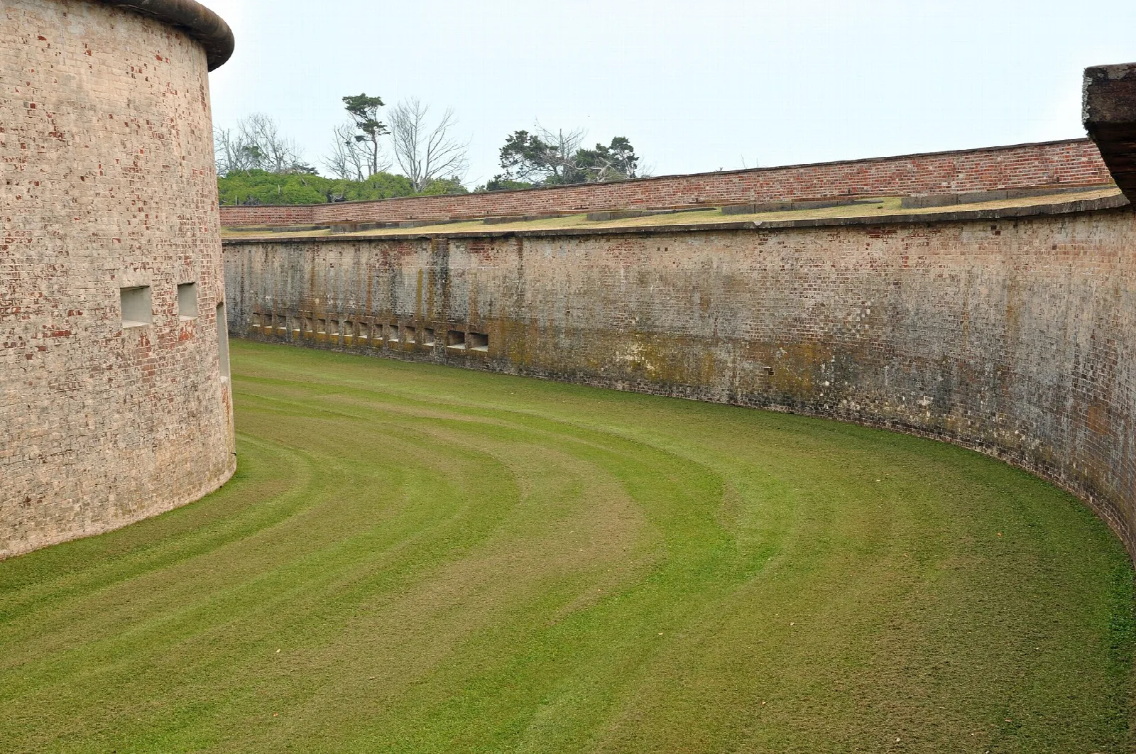 Curved brick fort wall beside a mown grass moat