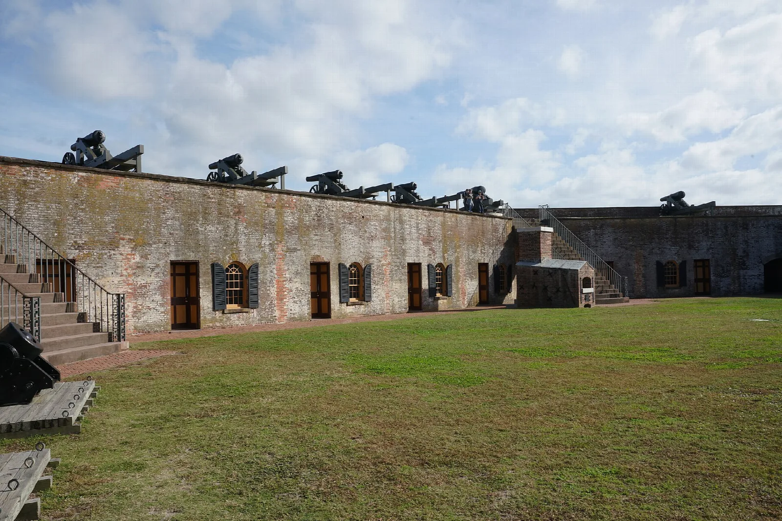 Brick fort wall with cannons along the top and a grassy courtyard below