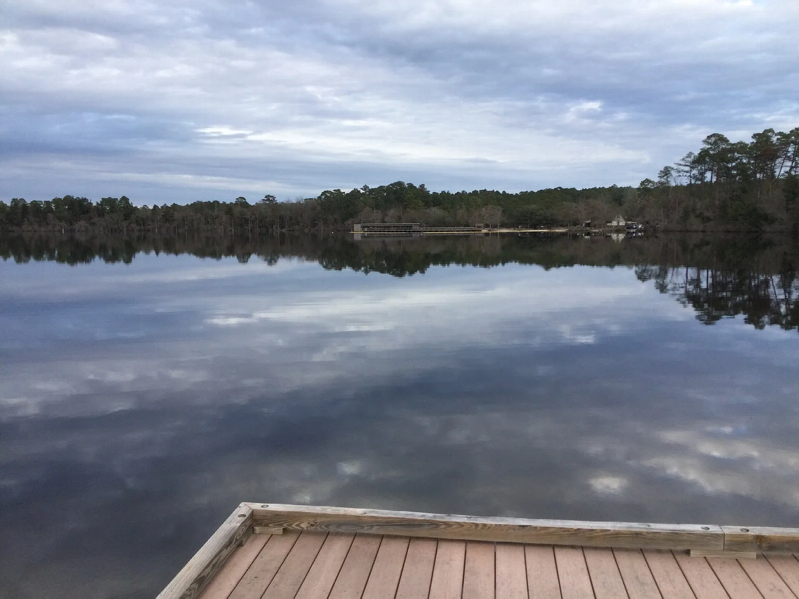 Corner of a wooden pier above still lake water under a cloudy sky