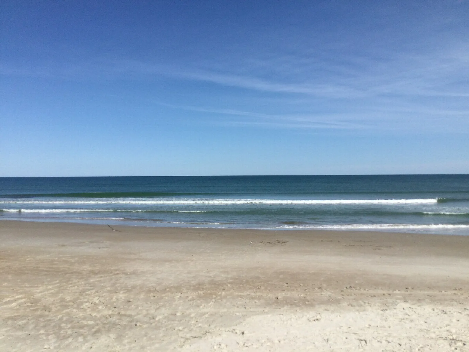 Empty sandy beach with waves rolling in under a blue sky