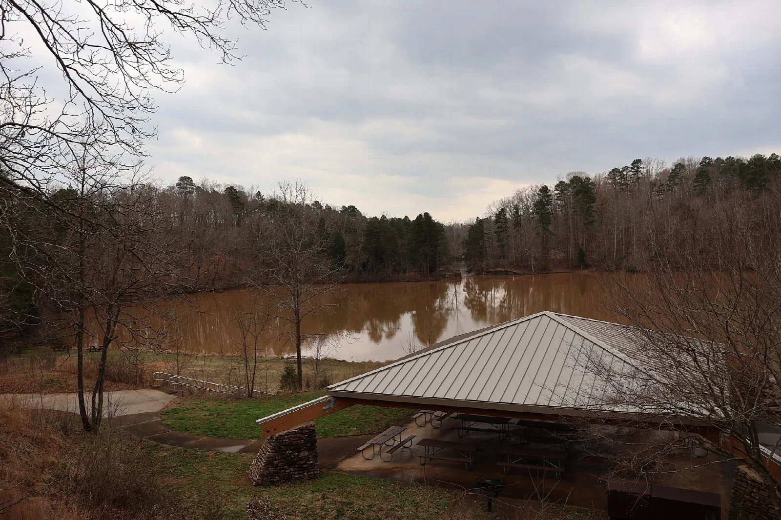 Metal-roofed picnic shelter beside a brown lake under a gray sky