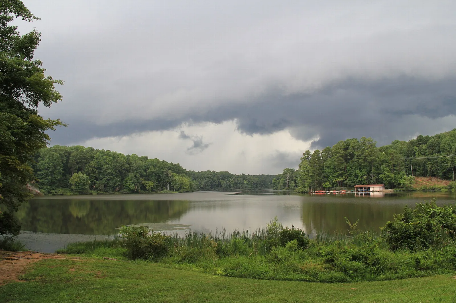Lake under dark storm clouds with a small boathouse among trees