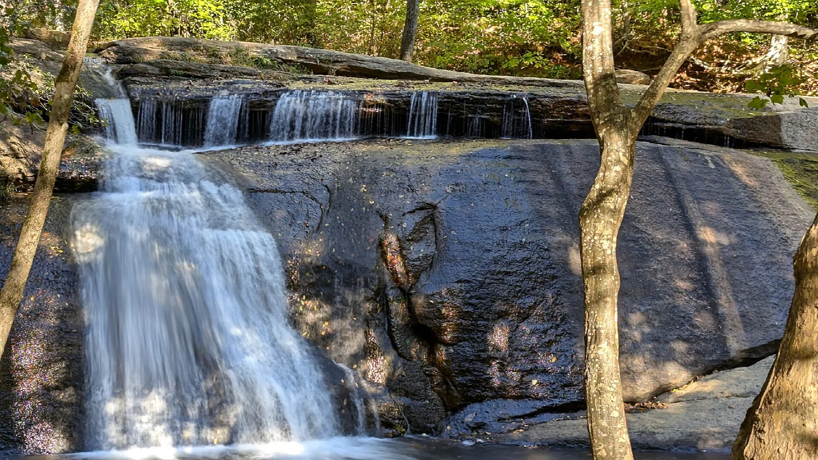 Long-exposure waterfall over a rock ledge with trees at the sides