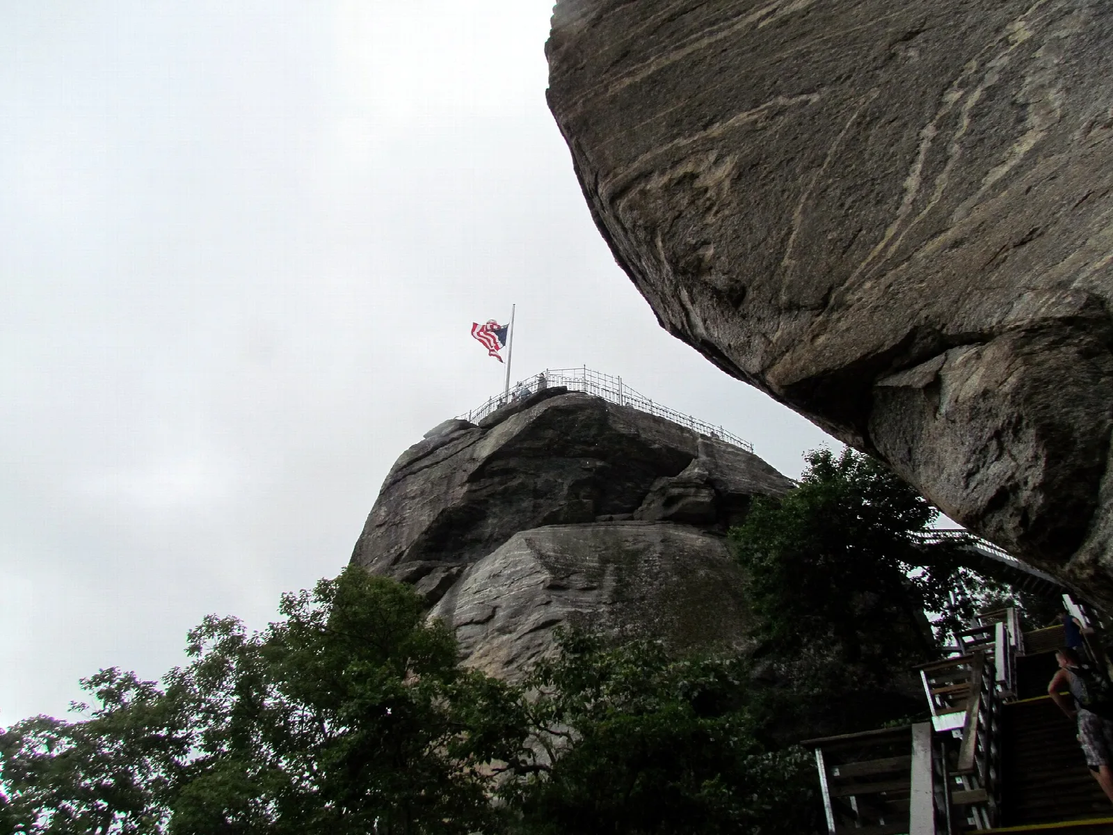 Rock spire with a flag on top under a large overhanging boulder