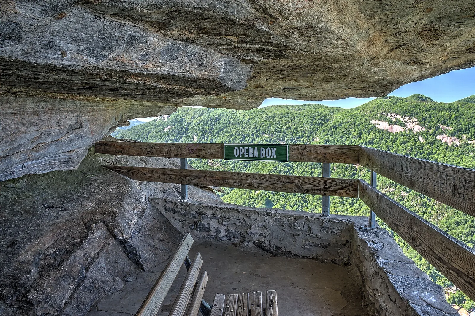 Wooden railing at a rock overhang looking out over forested ridges