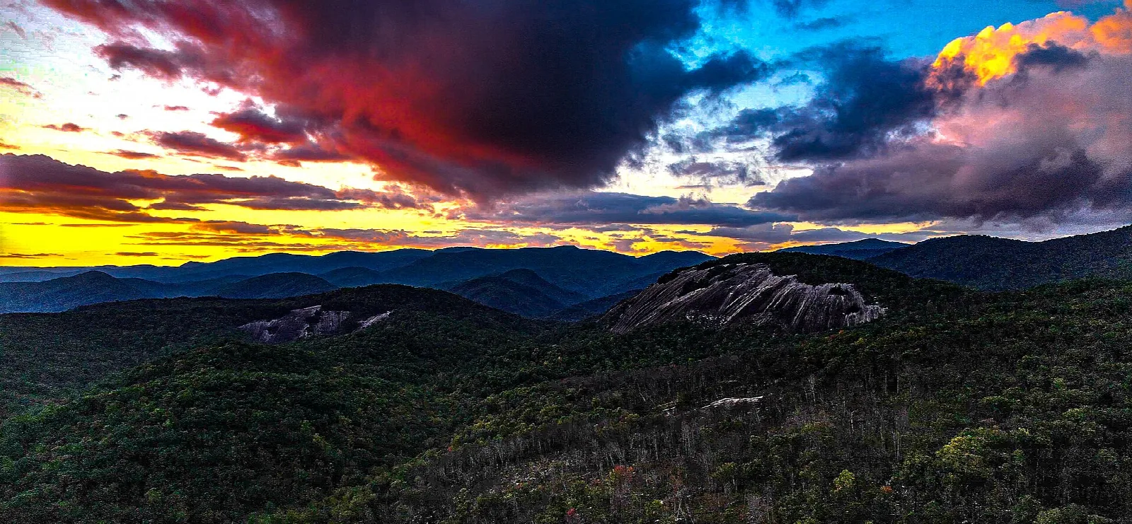 Dramatic sunset sky in red and orange over dark forested mountains