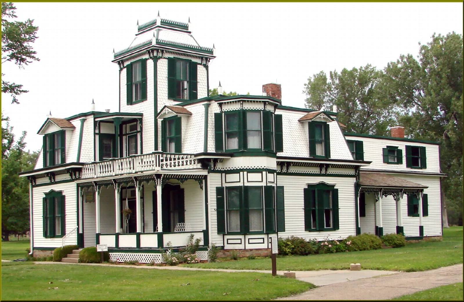 White two-story mansion with green shutters and a porch on a green lawn