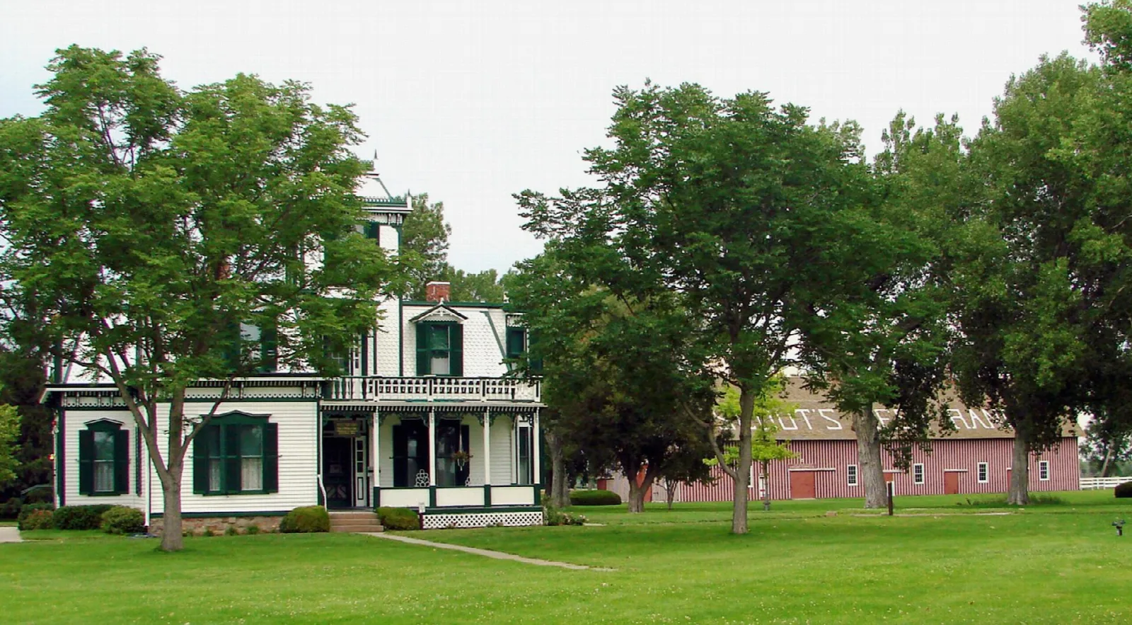 Ranch house among large trees with a red barn behind it