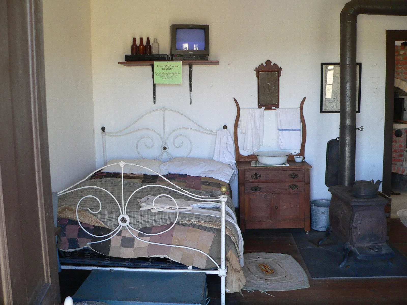 Bedroom with an iron bed, dresser and wood stove in a historic fort building