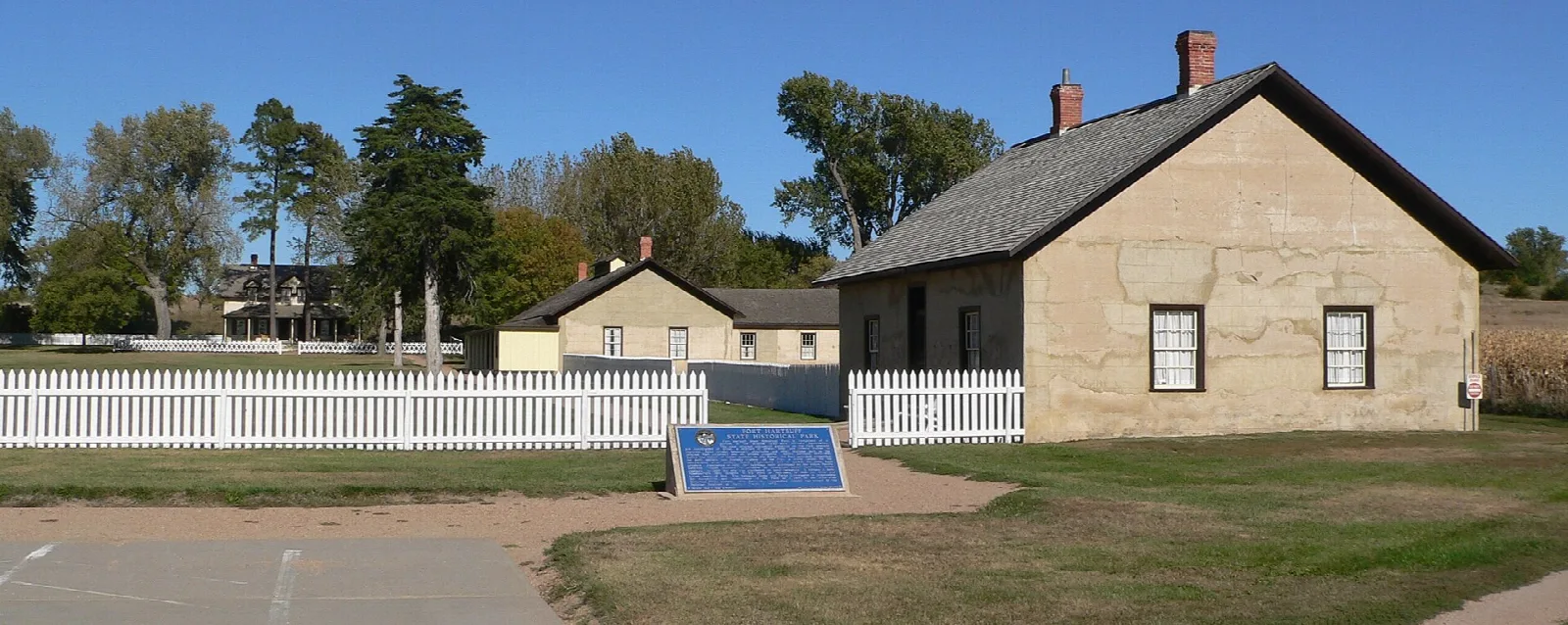 Tan building with a pitched roof beside a white picket fence under a blue sky