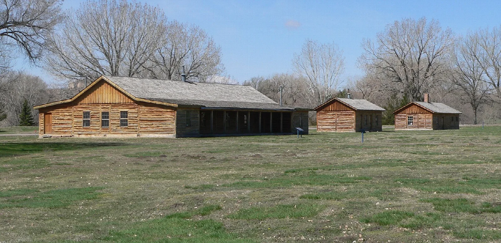 Row of log buildings on the old parade ground with bare trees behind