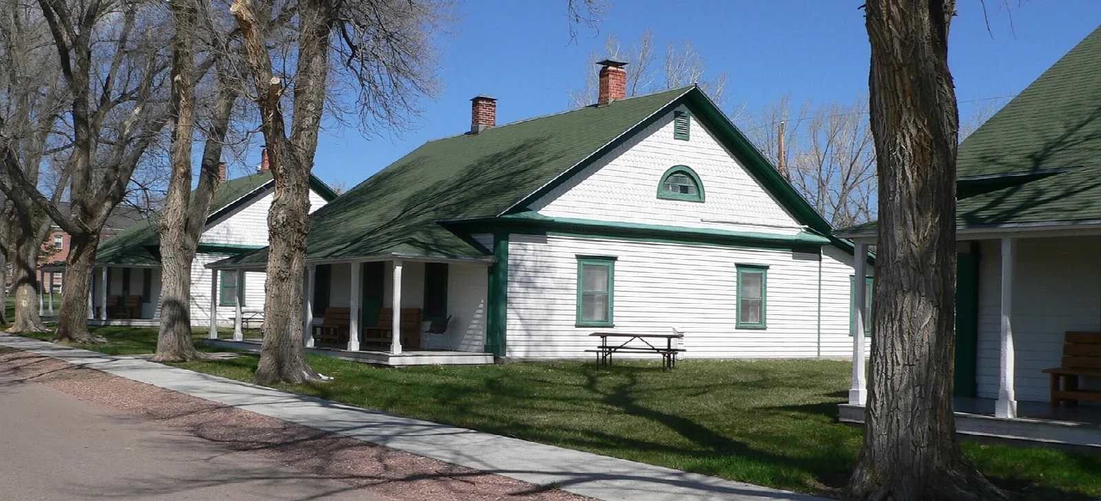 White officers' quarters with a green roof along a brick-lined street