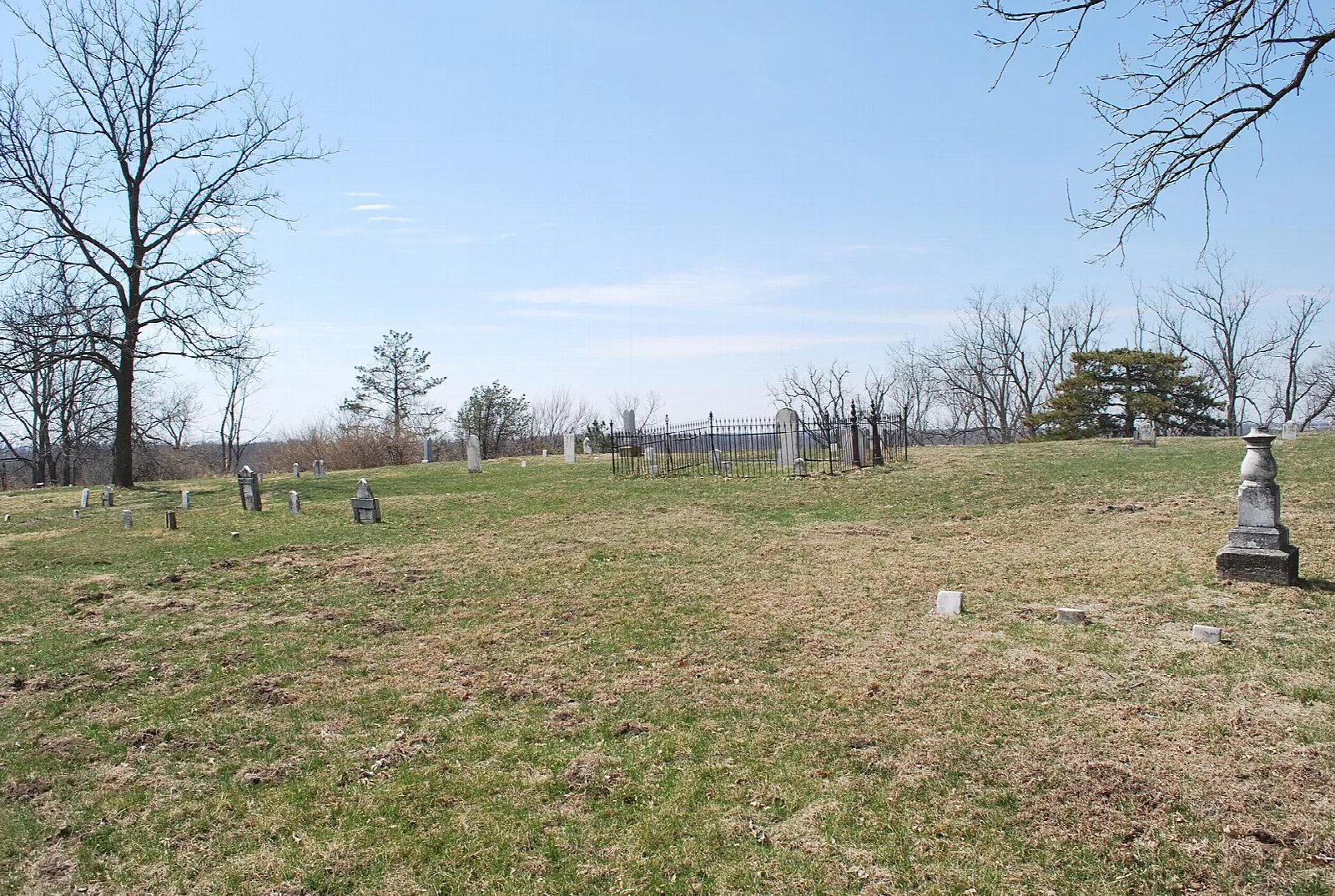 Grassy hilltop cemetery with old headstones and bare trees