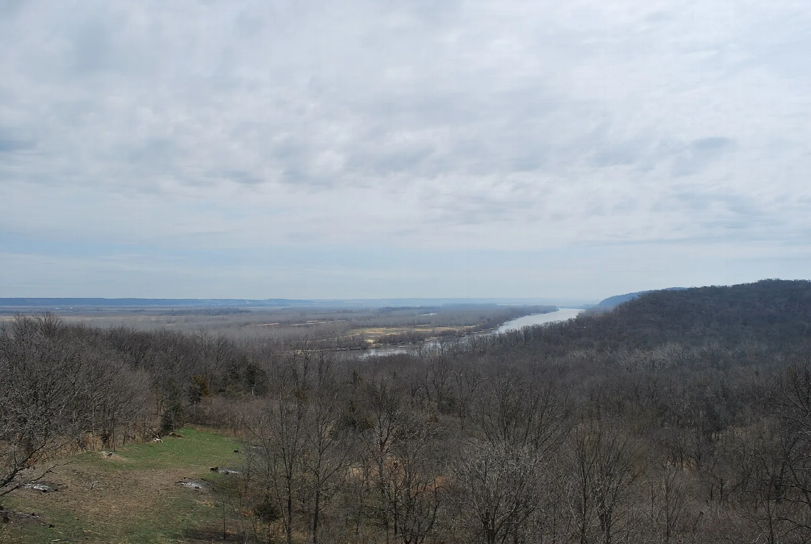 Wooded bluffs above a wide river valley under a cloudy sky