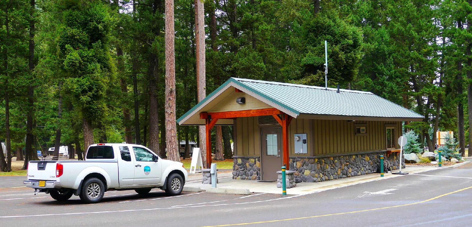 Small entrance station building with a truck parked beside it among tall pines