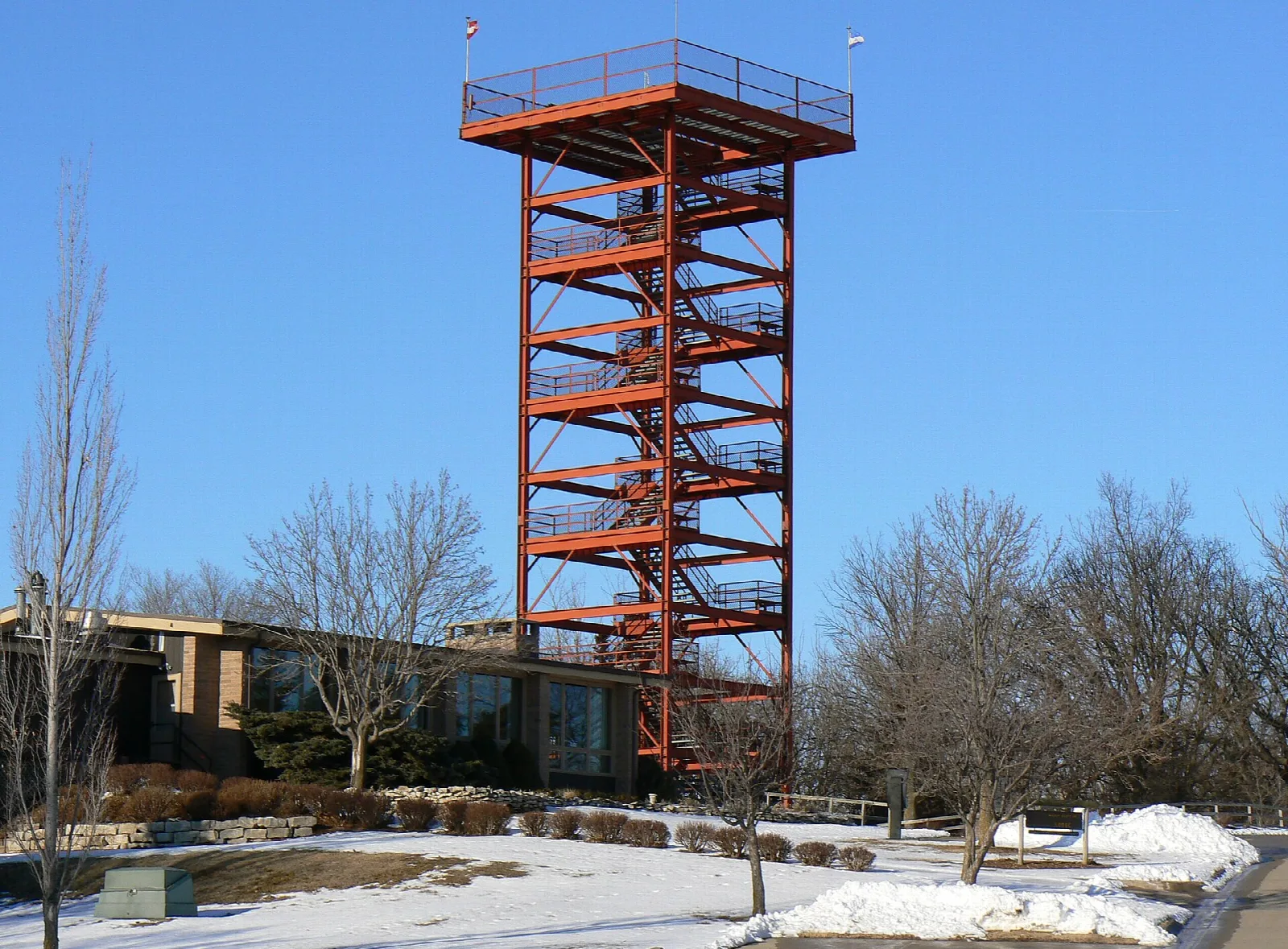 Tall orange steel observation tower beside a building, snow on the ground, blue sky