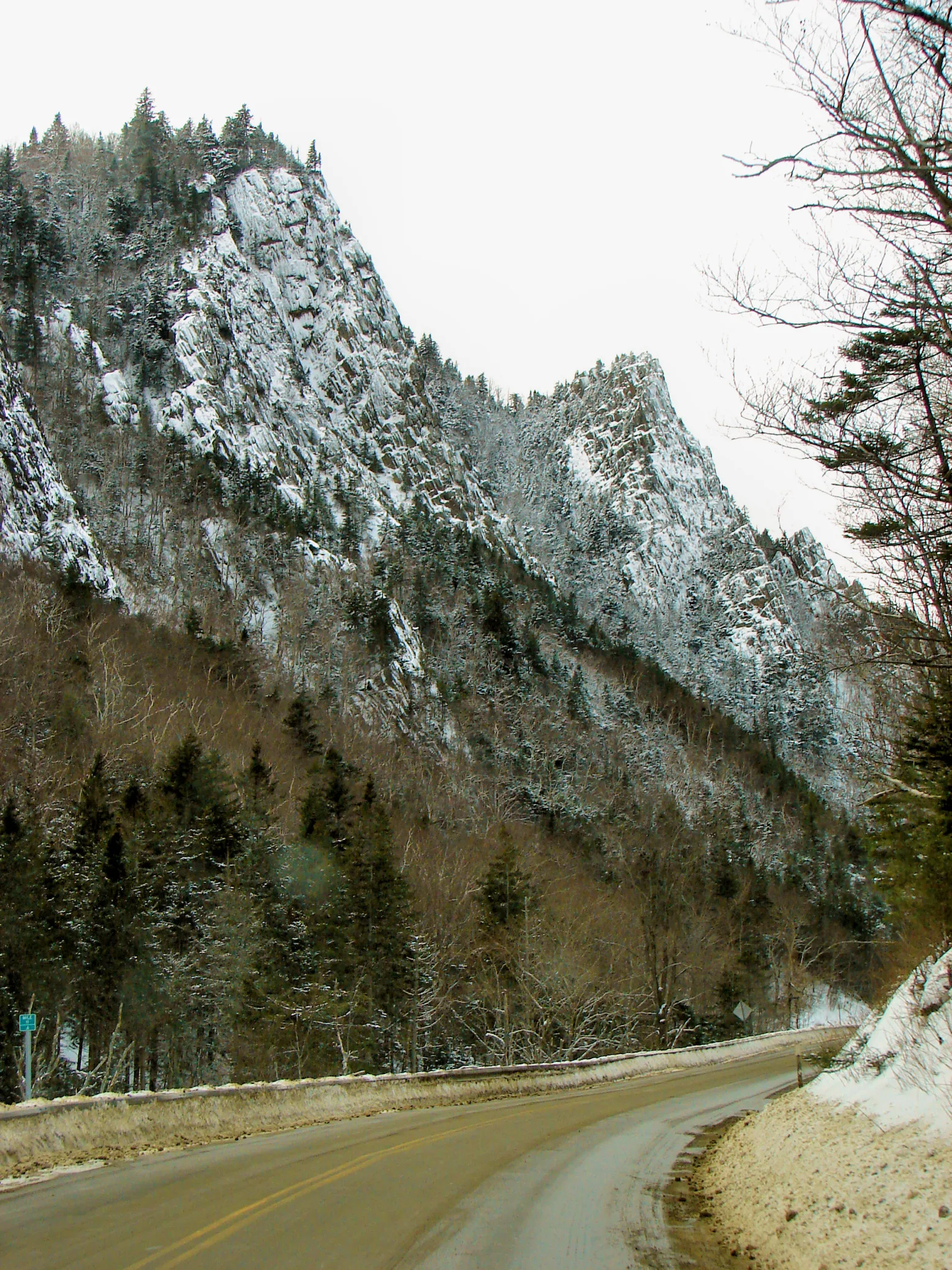 Road winding through a steep rocky notch with snow on the cliffs and roadside