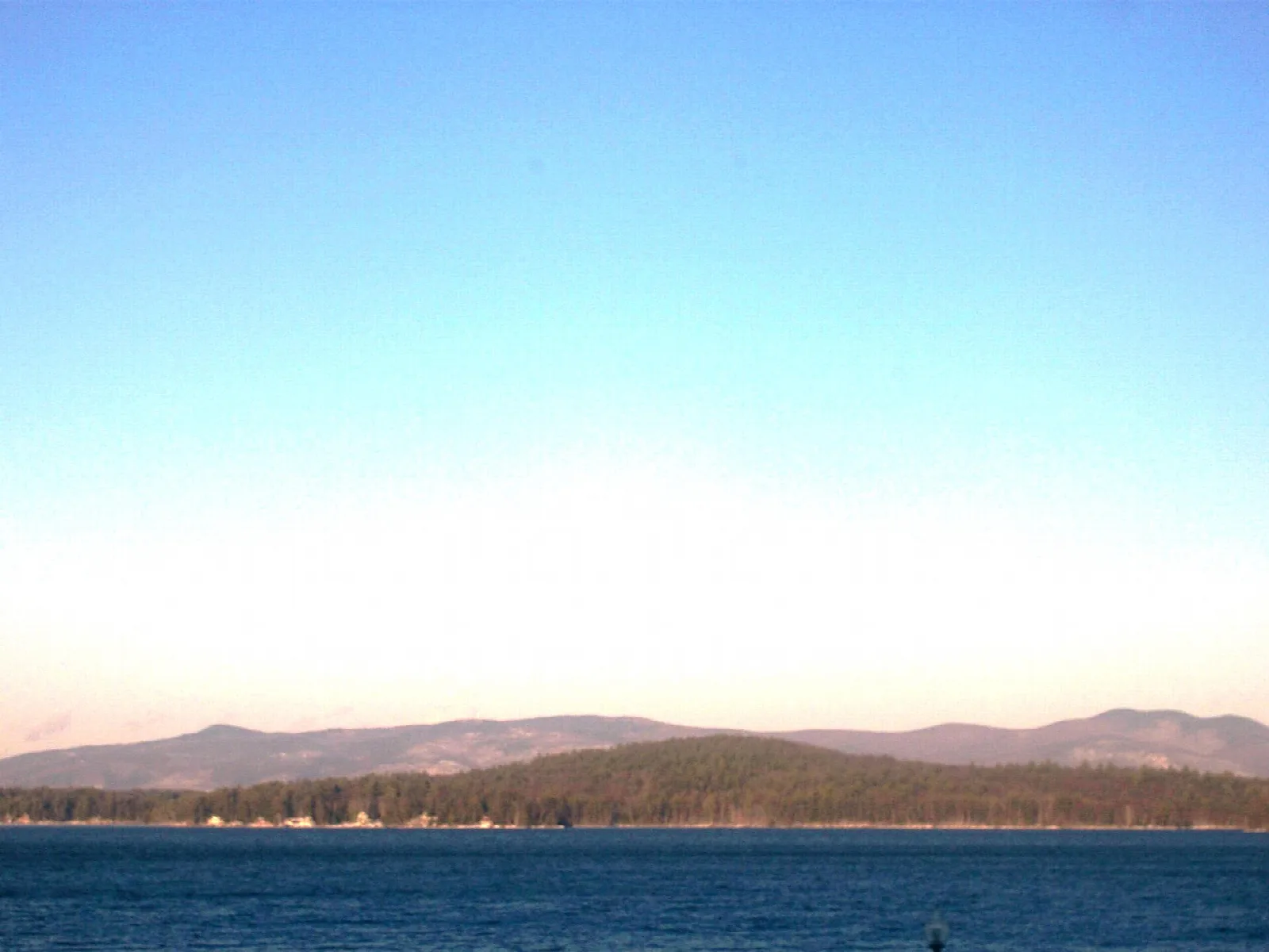 Wide blue lake with low forested hills along the far shore at dusk